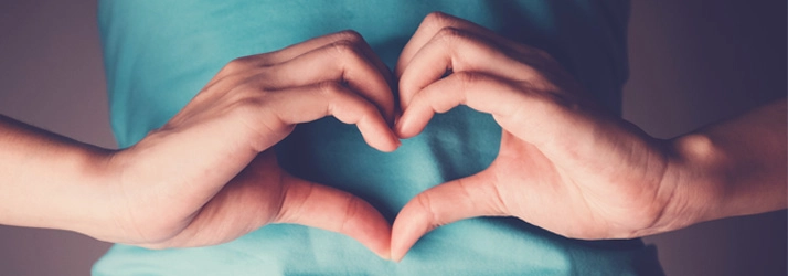 Person making heart hands over their stomach.